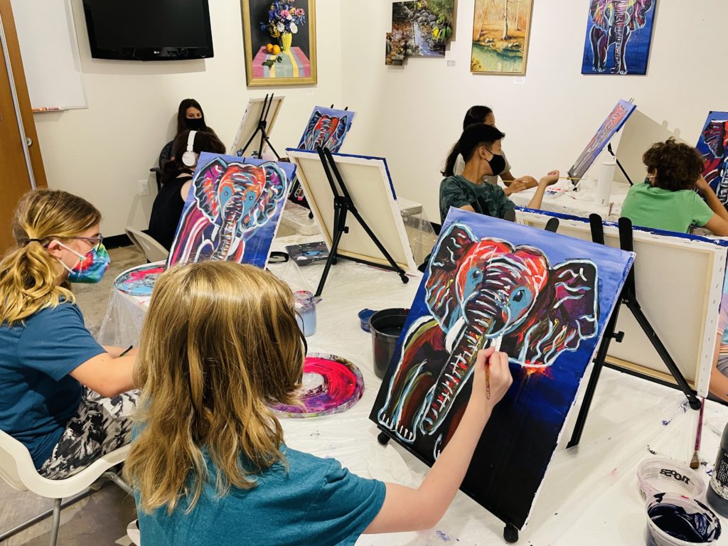 Middle school artists paint elephants on their canvases during art camp.