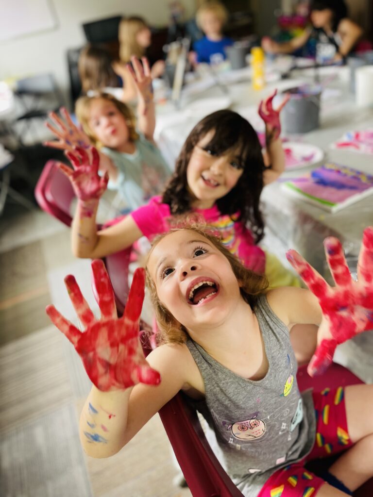 Kids laugh while posing for a picture with their hands covered in red paint