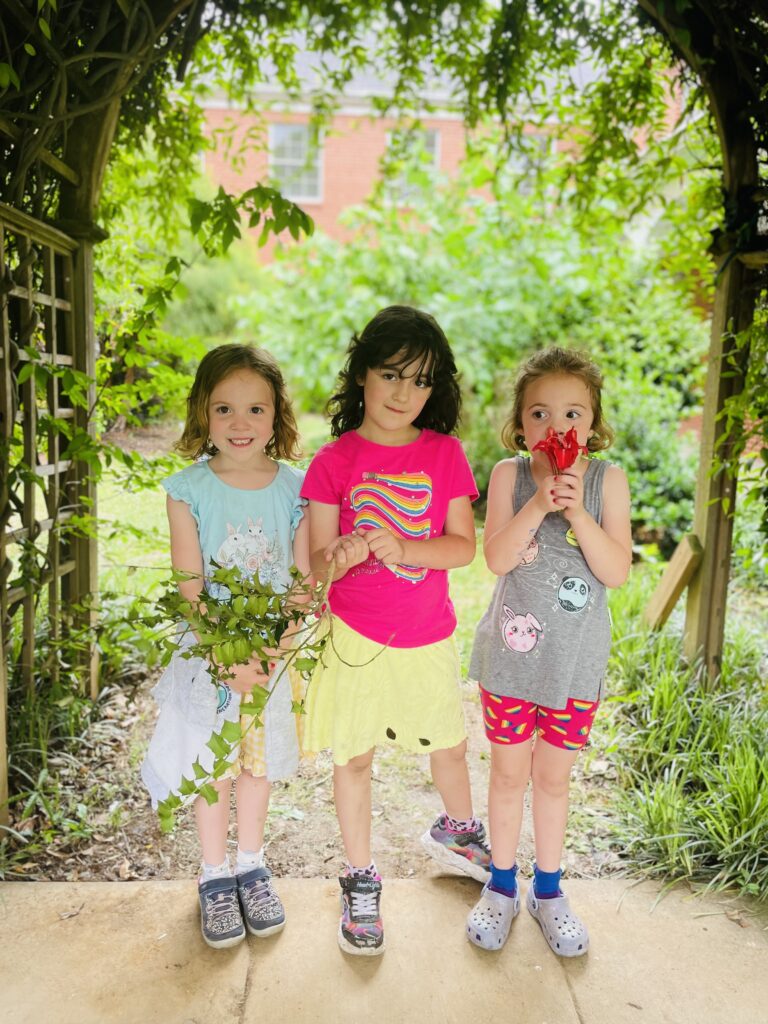 Three young girls pose with flowers under the trellis in the art camp courtyard.